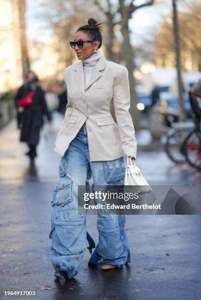Guest wears sunglasses, earrings, a white turtleneck wool knitted pullover, a white oversized blazer jacket, a white Hermes bag, blue flared cargo...
