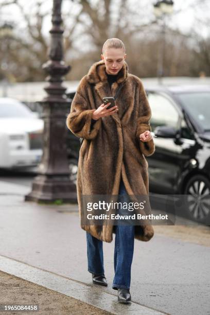 Model wears a brown long fur coat, blue jeans, black pointed leather shoes, outside Schiaparelli, during the Haute Couture Spring/Summer 2024 as part...