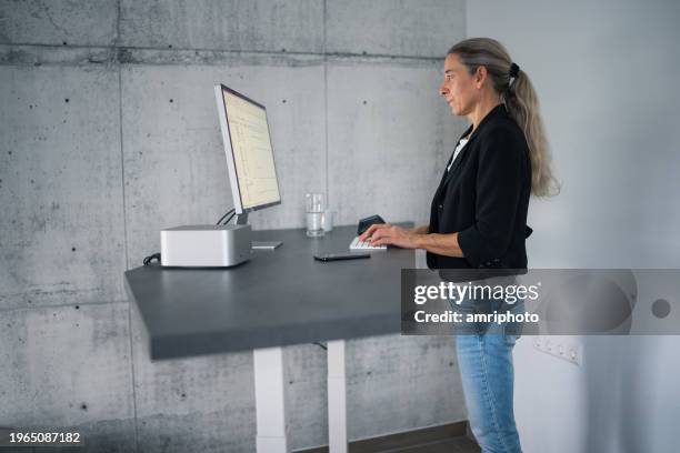 donna che lavora alla scrivania del computer in piedi regolabile in altezza nell'ufficio di casa - ergonomia foto e immagini stock