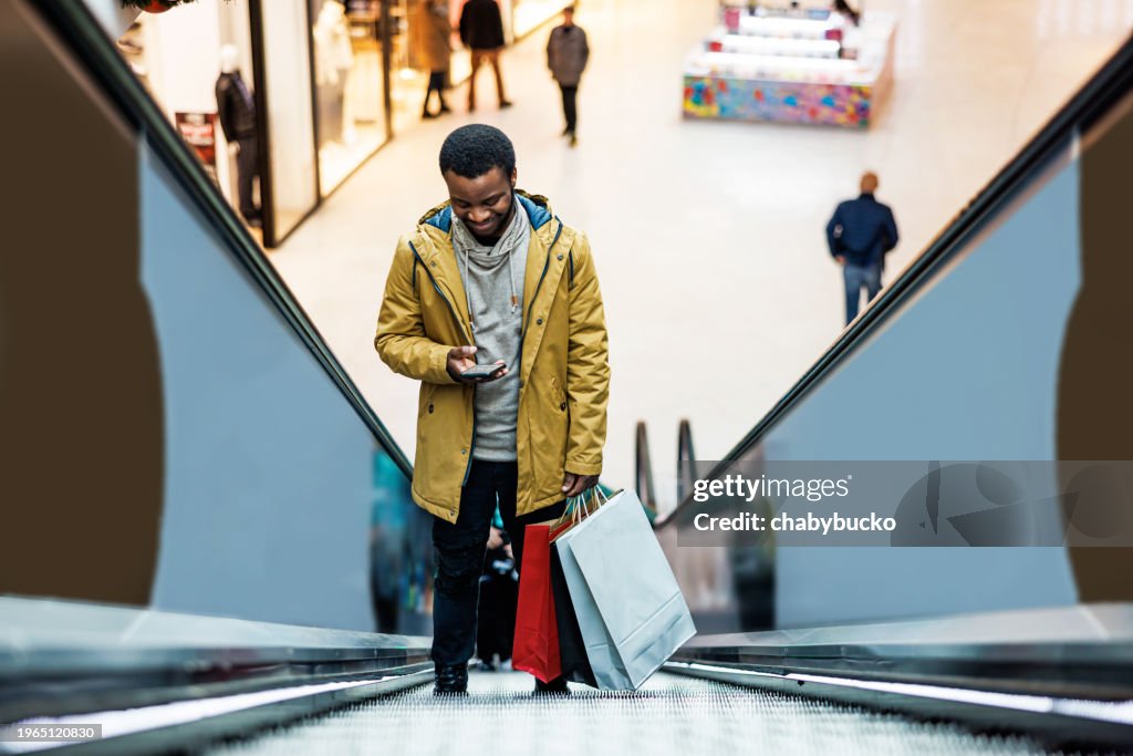 African American man using smartphone on escalator in shopping mall