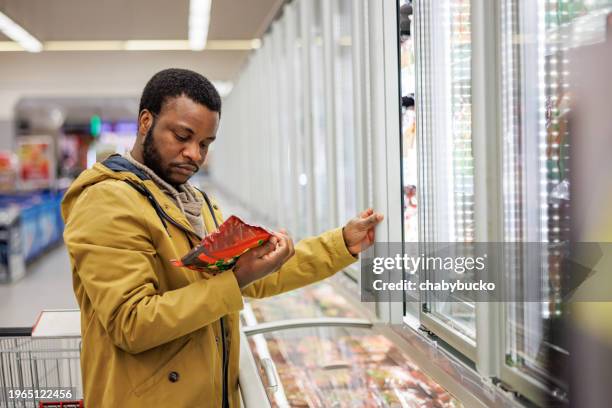 young man reads nutrition labels on frozen product - man buying groceries stock pictures, royalty-free photos & images