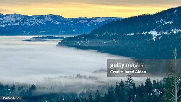 vast clouds over donner lake and truckee, mount rose in the background, horizon with yellow orange sky, forested hills rising above dense clouds and trees appearing through fog, view from donner pass, donner summit california - donner summit stock pictures, royalty-free photos & images