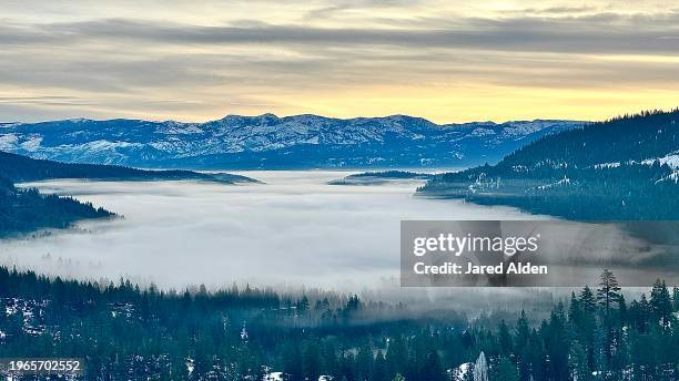 vast clouds over donner lake and truckee, mount rose in the background, horizon with yellow orange sky, forested hills rising above dense clouds and trees appearing through fog, view from donner pass, donner summit california - donner summit stock pictures, royalty-free photos & images