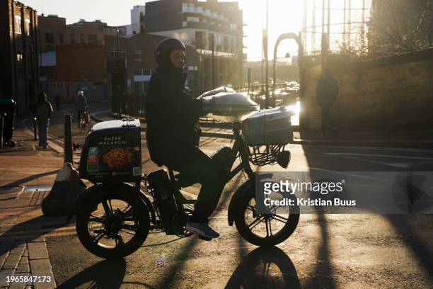Food delivery woman rides her bike in the early morning winter sun on the 26th of January 2024, London, United Kingdom.
