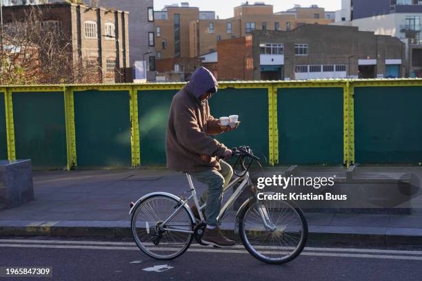 Bike rider with two cups of coffee in Hackney in the early morning winter sun on the 26th of January 2024, London, United Kingdom.