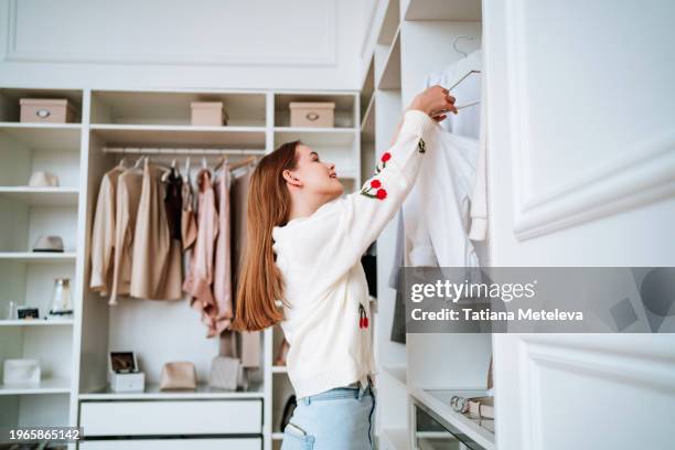 closet organization: young woman sorting through clothes on hanging racks in her personal wardrobe - dressing photos et images de collection