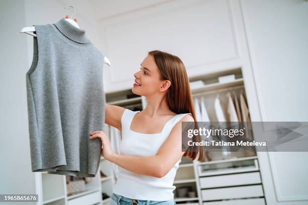 care of wool clothes. woman is holding a woolen vest, checking her clothes in walk-in closet - haut sans manches photos et images de collection