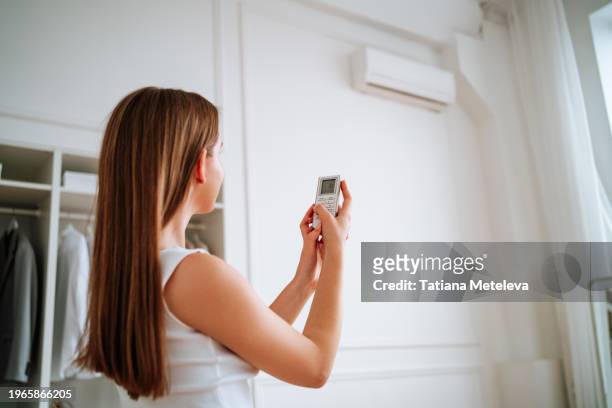 long haired woman with a remote control turns on the air conditioner for a comfortable indoor microclimate. - microclimate stock pictures, royalty-free photos & images