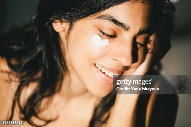 a beautiful asian woman enjoying a morning skincare routine, applying a sunblocking moisturizer to her skin - sun protection stock pictures, royalty-free photos & images