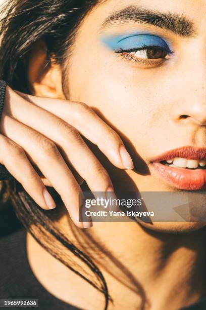 a conceptual fashionable portrait of a woman with bright blue eyeshadow against the sun - eye make up stock pictures, royalty-free photos & images