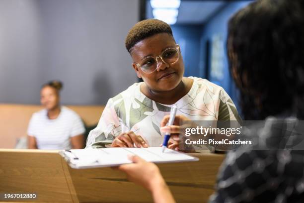 recepcionista de vista sobre el hombro explicando la forma a la mujer en la clínica médica - llenar el formulario fotografías e imágenes de stock