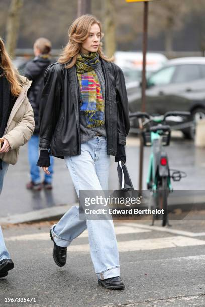 Model wears a yellow colored scarf, a black leather jacket, pale blue cuffed denim jeans pants, leather shoes, outside Chanel, during the Haute...