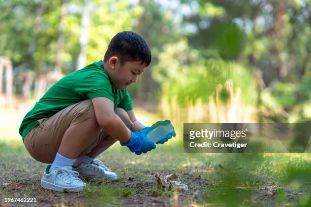 volunteer boy collects garbage - plastic bottles in public park. - kids with cleaning rubber gloves 個照片及圖片檔
