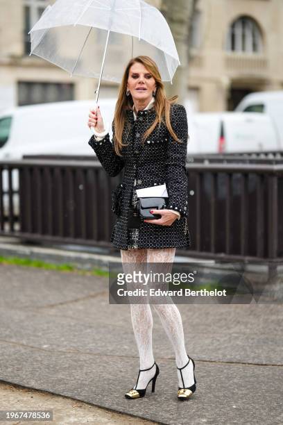 Anna Dello Russo wears a white shirt, earrings, a black jacket with printed geometric patterns , a black and white mini skirt, white tights with...
