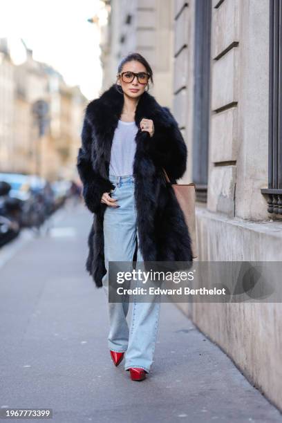 Heart Evangelista wears sunglasses, a black fluffy faux fur long coat, a white t-shirt, a blue denim jeans pants, red pointed shoes, during a street...