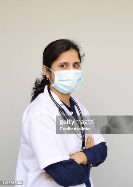 side view of one cheerful smiling woman or lady or female doctor portrait in surgical mask, and white lab coat and a stethoscope around her neck, eyes wide open, arms crossed over grey background with copy space for text - lady grey background bildbanksfoton och bilder