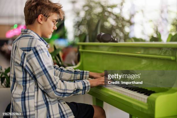 teenage boy playing on a green piano in a café - piano stock pictures, royalty-free photos & images