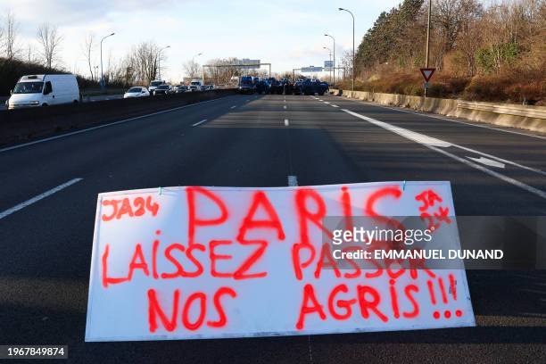 Banner reading "Paris, let our farmers pass" is seen in front of French CRS police officers standing beside French gendarmerie armoured personnel...