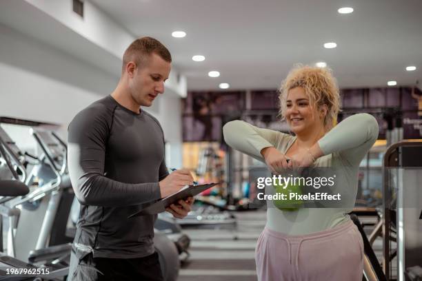plus size woman with her trainer working out with kettlebell - fitnessapparaat stockfoto's en -beelden