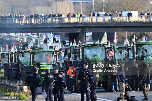 Police officers take security measures as French farmers form a convoy with their tractors and block the roads on the A6 Road as part of nationwide...