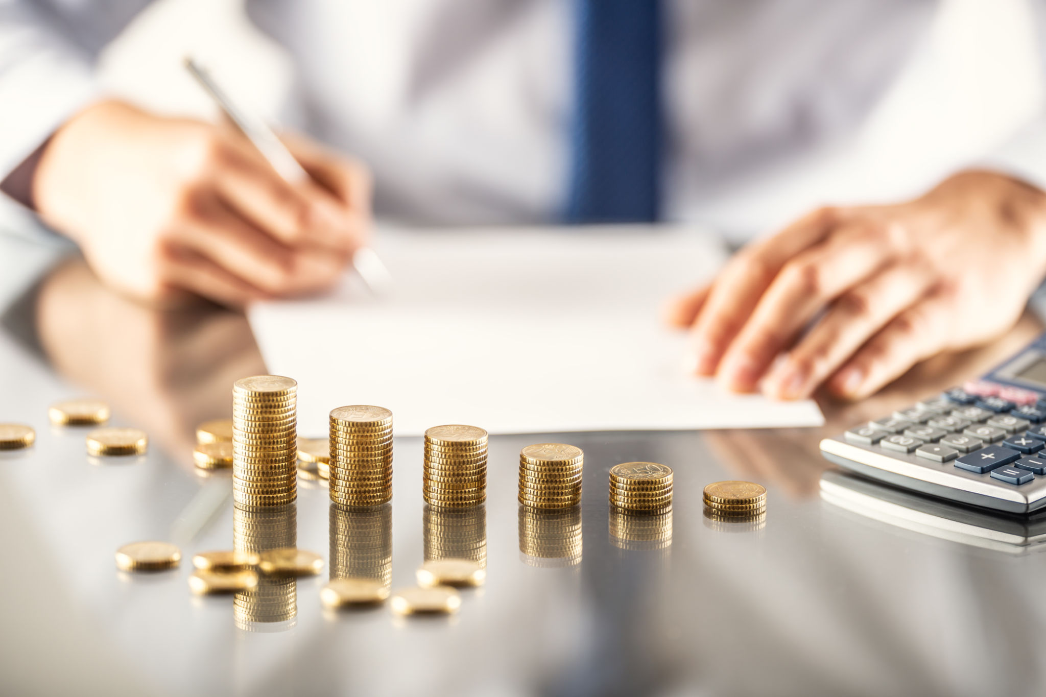 Business man signs a mortgage or insurance contract, gold coins in front of him in the form of a graph. Business man signs a mortgage or insurance contract, gold coins in front of him in the form of a graph.