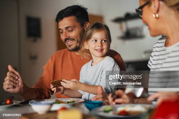 portrait of a happy little girl having breakfast with her mother and father at home - menselijke relaties stockfoto's en -beelden