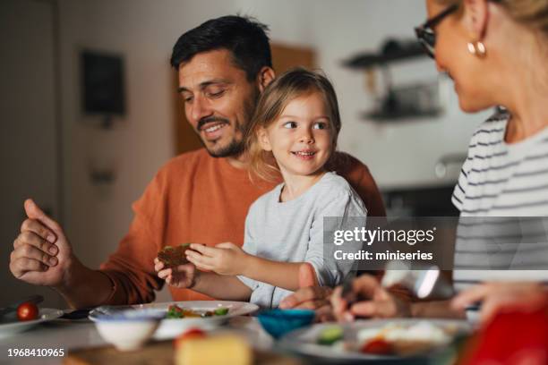 portrait of a happy little girl having breakfast with her mother and father at home - children eating breakfast stock pictures, royalty-free photos & images