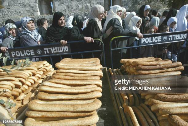 Palestinian women walk past stacks of traditional sesame bread rolls for sale at a stand near Jerusalem's Old City 15 November 2002. Security was...