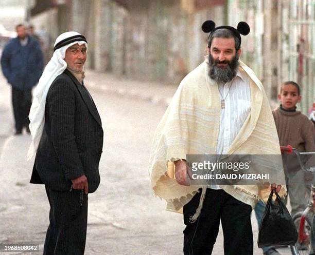 Jewish settler wearing Mickey Mouse ears on his kippa walks past Palestinians on the main street of the West Bank town of Hebron 10 January 1997....