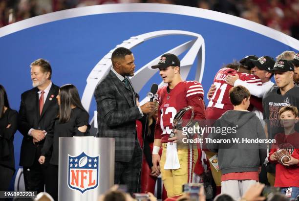 Brock Purdy of the San Francisco 49ers talks with Michael Strahan while holding the George Halas Trophy after defeating the Detroit Lions 34-31 in...