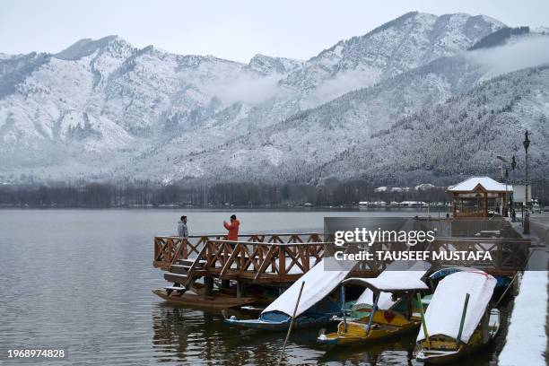 Man poses for a picture at Dal Lake with a backdrop of snow-covered mountains after the first snowfall of the winter in Srinagar on February 1, 2024.
