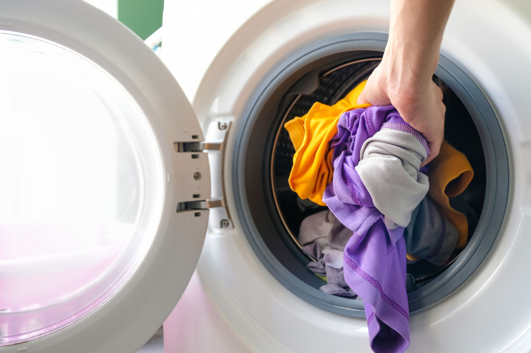 A woman opens the front door of a washing machine and puts clothes into the washing machine to clean and disinfect. Clean and healthy concept A woman opens the front door of a washing machine and puts clothes into the washing machine to clean and disinfect. Clean and healthy concept