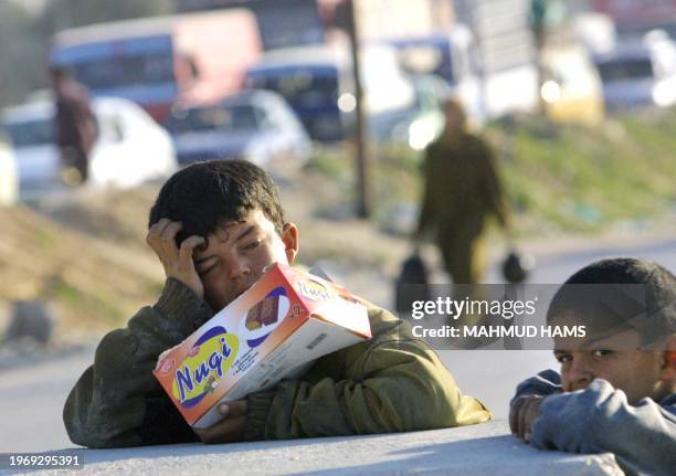 Palestinian boy selling sweets to passers by rests against a concrete block as vehicles queue at the Israeli manned Kfar Dorum checkpoint near the...