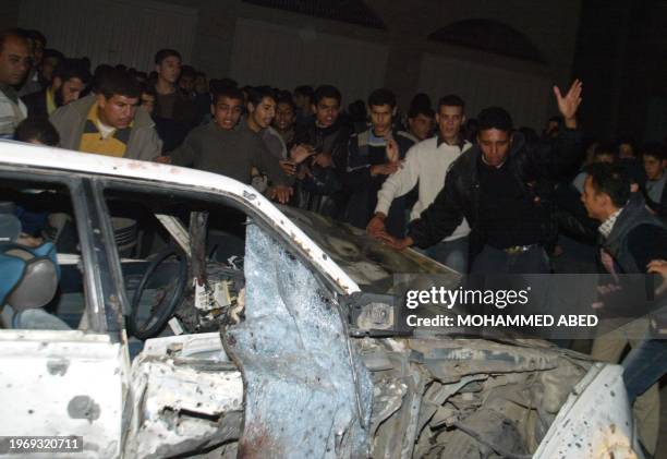 Palestinians gather around a wrecked car that was targeted by Israeli helicopter gunships at Al-Jalah Street, in a northern district of Gaza City, 25...