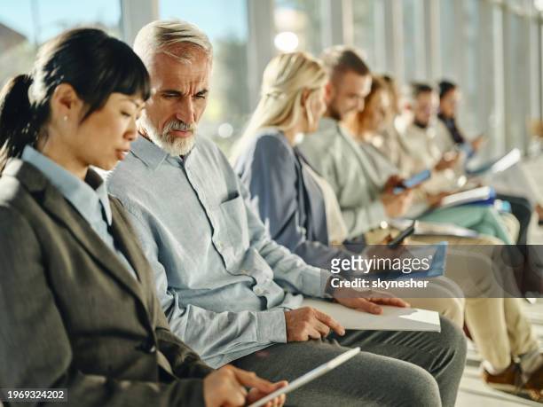 business colleagues using touchpad while waiting for job interview with other candidates. - lining up stock pictures, royalty-free photos & images