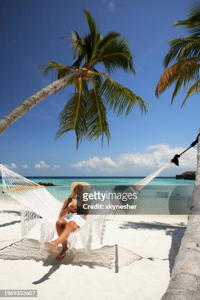 carefree woman having a drink in hammock on the beach. - meeru island stockfoto's en -beelden