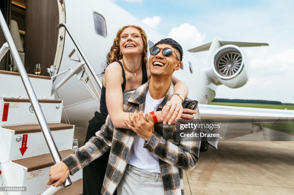 Young multiethnic couple enjoying travel by private jet. Young successful people in front of the private jet.