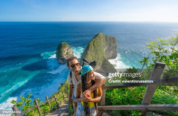 glückliches multiethnisches paar, das über dem strand von kelingking steht, die aussicht genießt und selfies macht - person gemischter abstammung stock-fotos und bilder