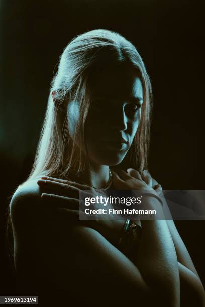 gorgeous woman looking straight in to the camera with bright turquoise light with her arms crossed on her collarbone. mystery cinematic portrait. - rim light portrait stock pictures, royalty-free photos & images
