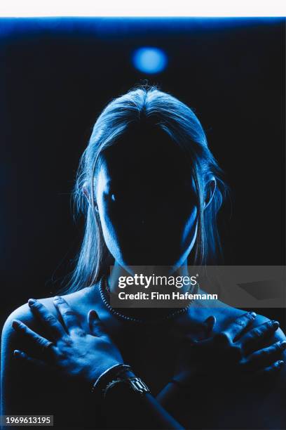 young woman  frontal portrait in blue light looking straight into the camera with her arms crossed on her collarbone. spooky. - rim light portrait stock pictures, royalty-free photos & images