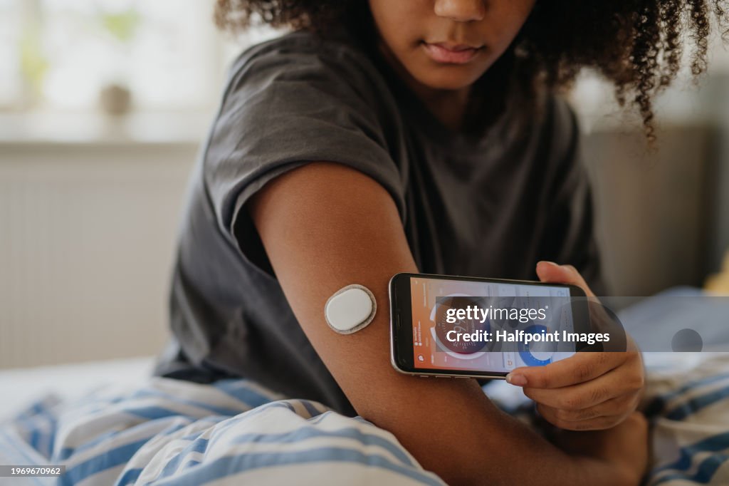 Teenage girl connecting smartphone to continuous glucose monitor, checking blood glucose first thing in the morning.