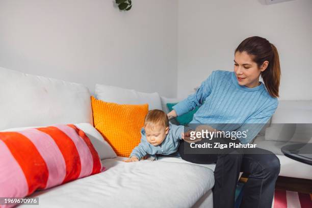 young mother with baby son on sofa at home. learning to walk, showing love to each other. - ziga plahutar stock pictures, royalty-free photos & images