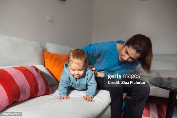 young mother with baby son on sofa at home. learning to walk, showing love to each other. - ziga plahutar stock pictures, royalty-free photos & images