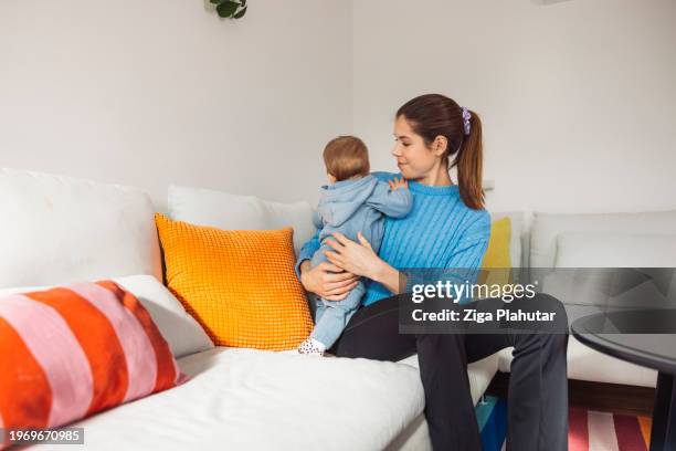 young mother with baby son on sofa at home. learning to walk, showing love to each other. - ziga plahutar stock pictures, royalty-free photos & images