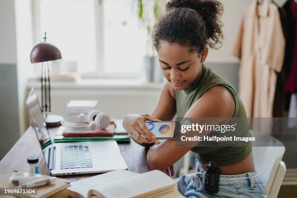 teenage girl connecting smartphone to continuous glucose monitor, checking blood glucose during day. student doing routine blood check while studying. - fühler stock-fotos und bilder