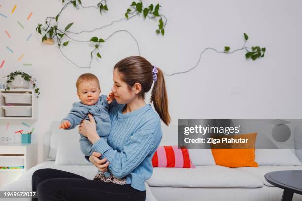 young mother with baby son on sofa at home. learning to walk, showing love to each other. - ziga plahutar stock pictures, royalty-free photos & images