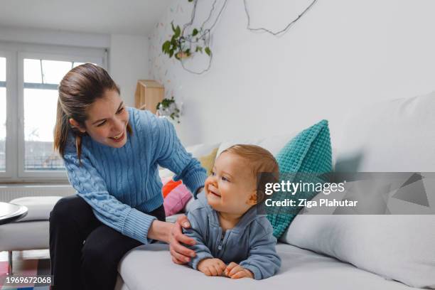 young mother with baby son on sofa at home. learning to walk, showing love to each other. - ziga plahutar stock pictures, royalty-free photos & images