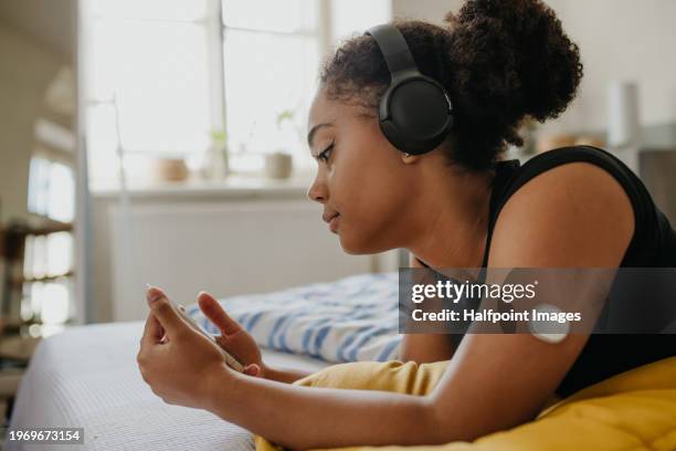 teenage diabetic lying on bed and scrolling on smartphone, feeling lonely and depressed. teenage girl feeling different from friends, have body image issues because of insulin pump and cgm. - smoking patch stock pictures, royalty-free photos & images