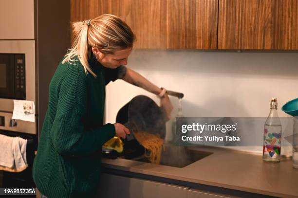 jeune femme vidant l’eau des spaghettis. - égouttoir photos et images de collection