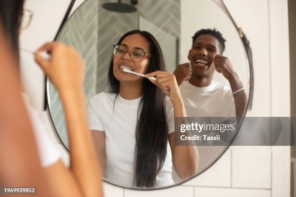 happy couple, mirror and cleaning teeth for dental hygiene or grooming in bathroom together at home. face of man and woman with toothbrush and floss for tooth whitening, oral and gum care at house - brushing stock pictures, royalty-free photos & images